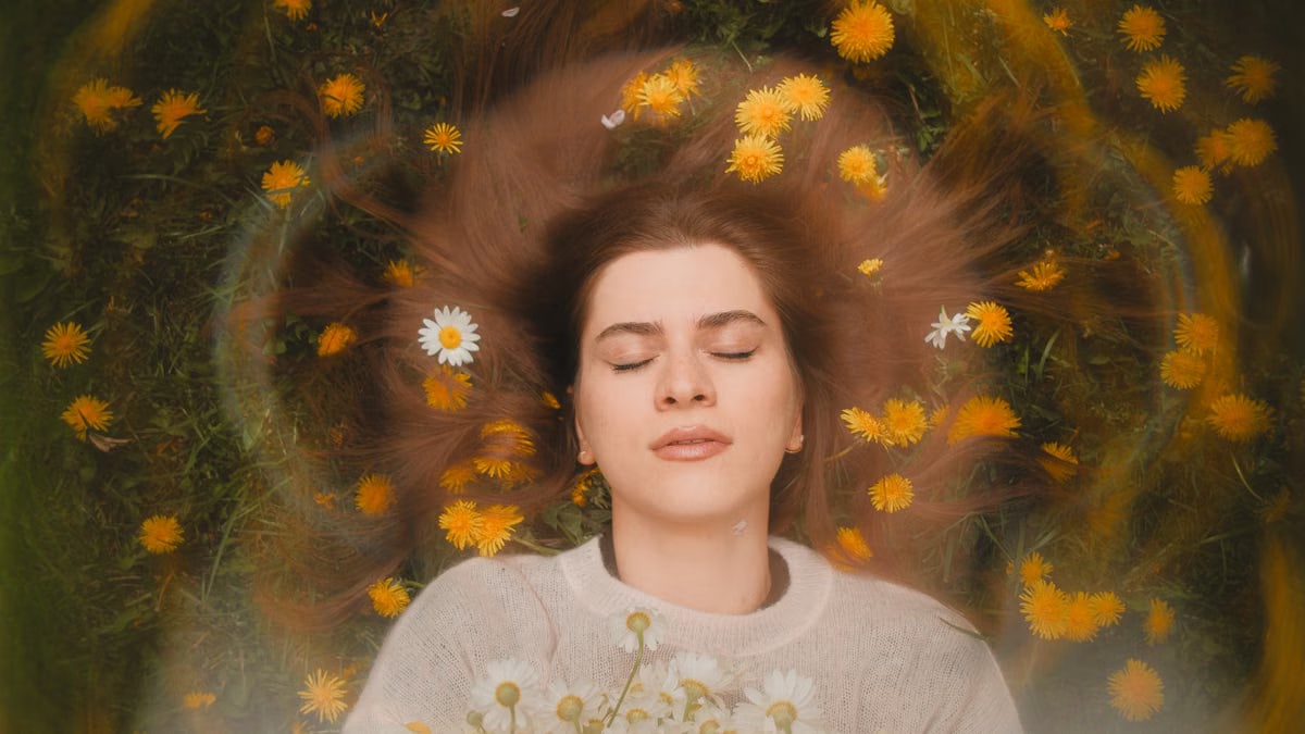 Relaxed woman with closed eyes, surrounded by daisies and dandelions, embracing nature's beauty.